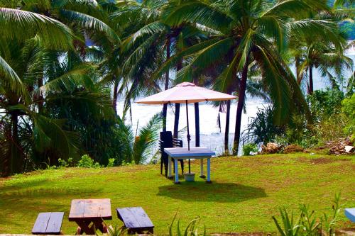 a table with an umbrella and a chair and two benches at Emma's Sea View in Hiriketiya