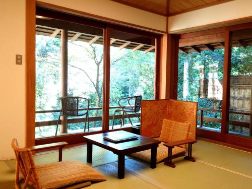 a living room with a table and chairs and windows at Hanafubuki in Ito
