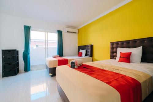 1 dormitorio con 2 camas y pared amarilla en RedDoorz at Kawaii Apartment Jimbaran, en Balian