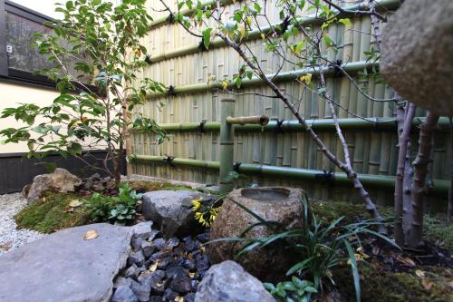 a bamboo fence with a tree and rocks at Brian Private Machiya in Higashiyama in Kyoto