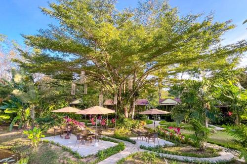 einen Garten mit Tischen, Sonnenschirmen und Bäumen in der Unterkunft Baan Bua Cottage SHA EXTRA PLUS B5510 in Ko Kood