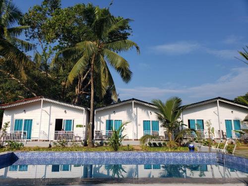 a row of white buildings with palm trees and a pool at White Truffle Resort, Arambol in Arambol