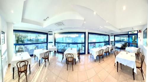 a restaurant with white tables and chairs and windows at Hotel Venere in Cesenatico