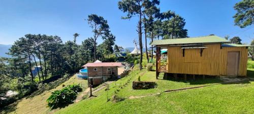 a small house on a grassy hill with trees at Odyssey Stays Umbir, Umiam Lake in Mawlyngkhung