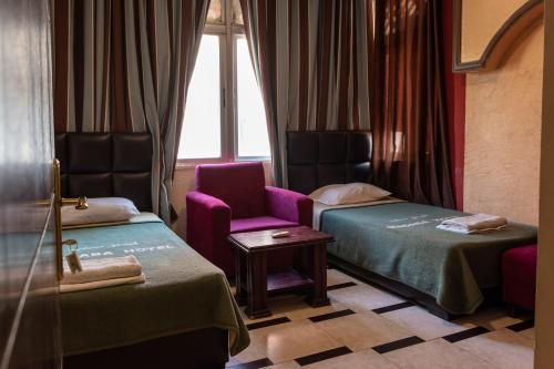 a room with two beds and a chair and a window at Madaba Hotel in Madaba