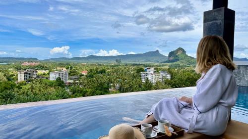 a woman sitting on the edge of a pool looking out at the city at Aonang Phu Dahla Private Pool & Sea View - SHA Plus in Ao Nang Beach