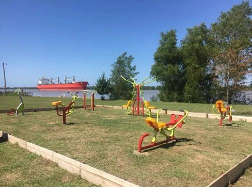 a group of playground equipment in a park with a ship in the background at CARELHUE GUAZU 1 in Villa Paranacito