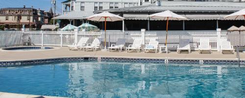 a swimming pool with white chairs and umbrellas at The Inn Of Cape May in Cape May