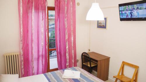 Habitación con mesa y ventana con cortinas rosas. en Colazione Inclusa - B&B Meteora, en Capurso