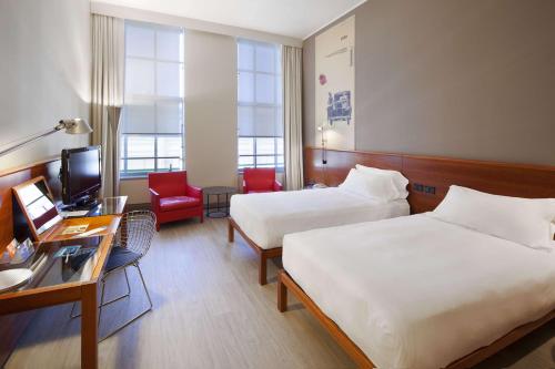トリノにあるNH トリノ リンゴット コングレスのベッド2台とデスクが備わるホテルルームです。