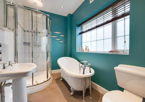 een badkamer met blauwe muren, een bad en een wastafel bij CowPasture Cottage in Felixstowe