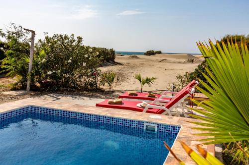 a swimming pool with two lawn chairs and a beach at Casa Killa Vichayito in Vichayito