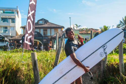 a man is holding a surfboard on the beach at Longboard Paradise Surf Club in Rio de Janeiro