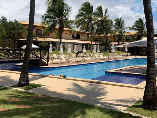 una piscina con sillas y palmeras y un edificio en Itacimirim vilage Villas da Praia en Itacimirim