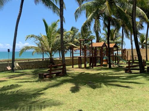 Itacimirim vilage Villas da Praia في إيتاسيميريم: حديقة بها ملعب مع أشجار النخيل والمحيط
