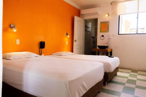 two beds in a room with an orange wall at Hotel Miami SM in Santa Marta