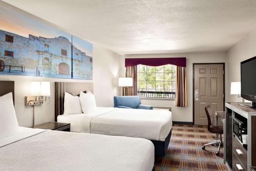 a hotel room with two beds and a flat screen tv at Days Inn by Wyndham San Antonio Near Fiesta Park in San Antonio