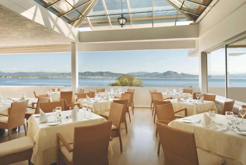 a restaurant with tables and chairs and a view of the ocean at Wyndham Loutraki Poseidon Resort in Loutraki