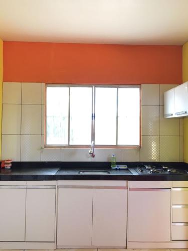 a kitchen with white cabinets and an orange wall at Lençóis Hospedagens in Barreirinhas