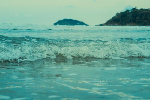 a small wave in the ocean with an island in the background at Pousada Acqua Bella PISCINA CLIMATIZADA in Bertioga
