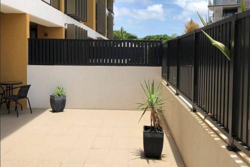 a patio with two potted plants and a fence at Darwin Waterfront Short Stay Apartments in Darwin