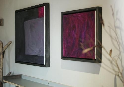 two framed paintings on a wall next to a shelf at Kaia Gallery Hotel Hoi An in Hoi An
