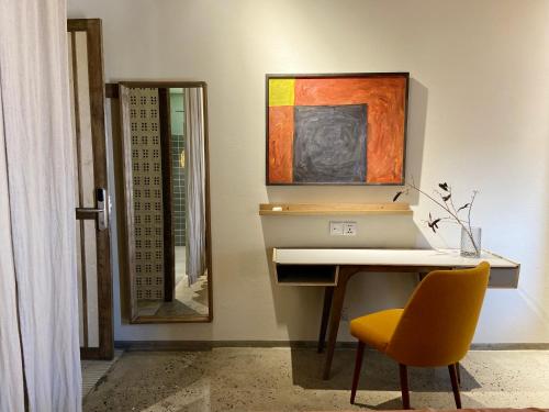 a desk with a yellow chair and a painting on the wall at Kaia Gallery Hotel Hoi An in Hoi An