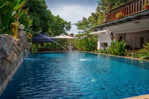 a swimming pool with an umbrella next to a house at Antonios Villa Hotel in Siem Reap