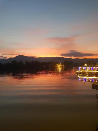 a sunset on a lake with lights on the water at The Hideaway in Kampot