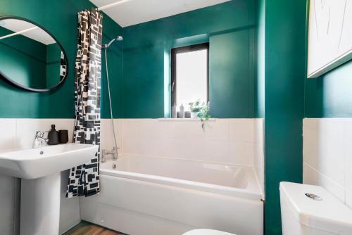 baño con paredes verdes, bañera y lavamanos en Townhouse in Ebbsfleet sleeps 9 with free parking, en Greenhithe