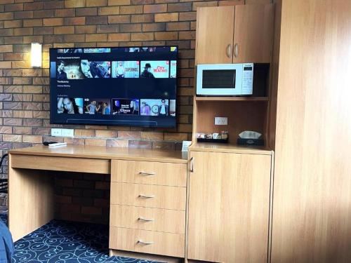 a living room with a tv and a desk with a microwave at Shiralee Motel Guyra in Guyra