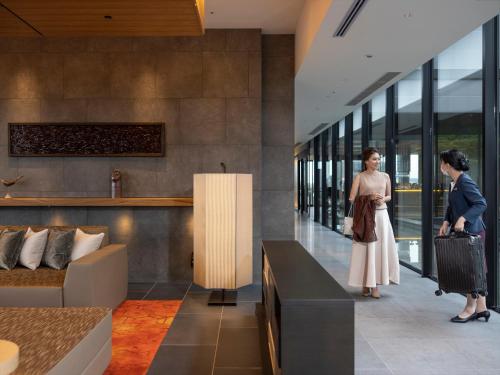 une femme debout dans un hall avec une valise dans l'établissement THE BLOSSOM KUMAMOTO, à Kumamoto