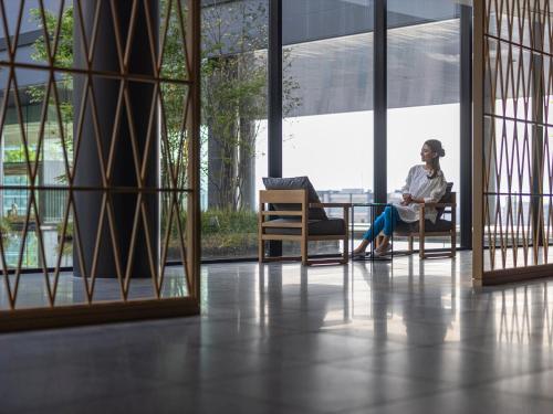 a woman sitting in a chair in a room with windows at THE BLOSSOM KUMAMOTO in Kumamoto
