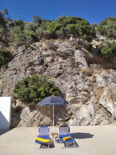 two chairs and an umbrella on a beach at MARINOS House WANDERN&ENTSPANNEN am Fusse des Psiloritis in Kamárai