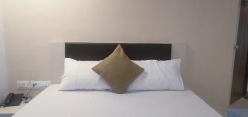 a bed with a brown pillow on top of white pillows at Hotel Success Residency in Ghansoli