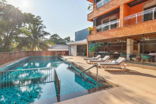 una piscina con tumbonas junto a un edificio en Aiden by best Western Vagator Goa, en Goa Velha