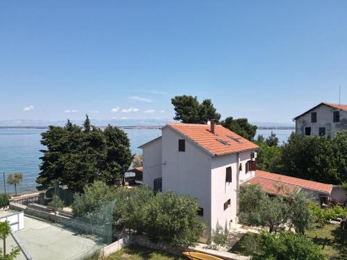 a white building with a red roof next to the water at Beachfront apartments Calm Sea in Preko