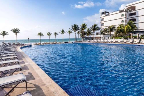 a swimming pool with chairs and the ocean in the background at Grand Residences Riviera Cancun, All Inclusive in Puerto Morelos