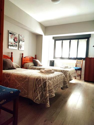 a bedroom with two beds and a table and windows at PENSIÓN PESQUERO in Burgos