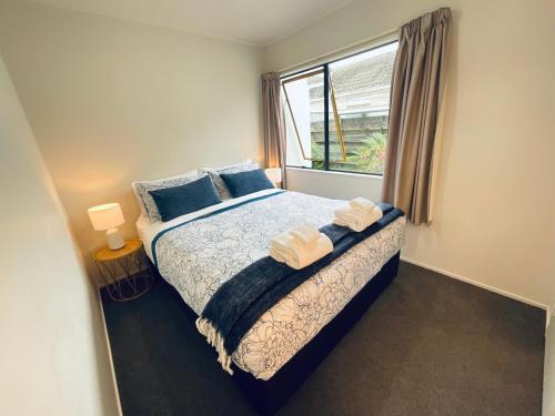 a bedroom with a bed with blue pillows and a window at Aintree On The Park in Mount Maunganui