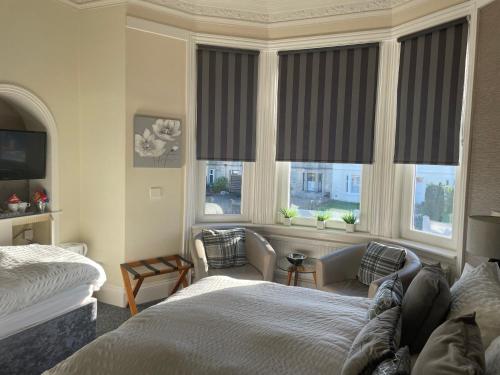a bedroom with a bed and a couch and windows at Beechwood Ensuite Guest House in Ayr