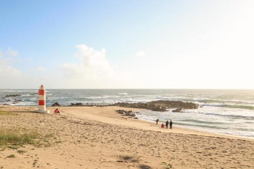 a lighthouse on a beach with a group of people at Casa Fragosa - Alojamento local in Póvoa de Varzim