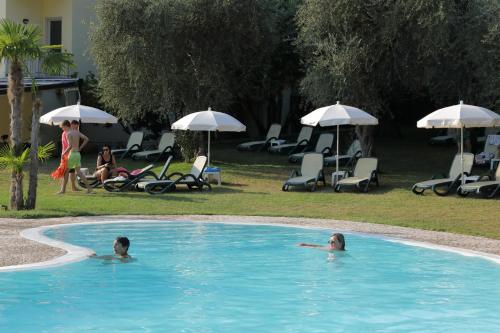 two people swimming in a swimming pool with umbrellas at Eco Hotel Benacus in Malcesine