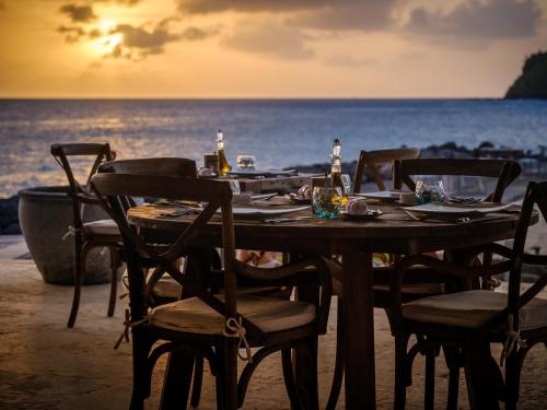 a wooden table on the beach with chairs and the ocean at The Liming Bequia in Friendship