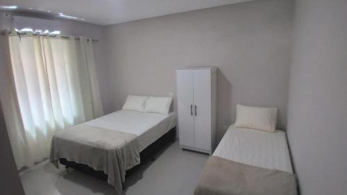 Cette chambre blanche comprend 2 lits et une armoire. dans l'établissement Casa aconchegante com piscina e bem localizada, à Foz do Iguaçu