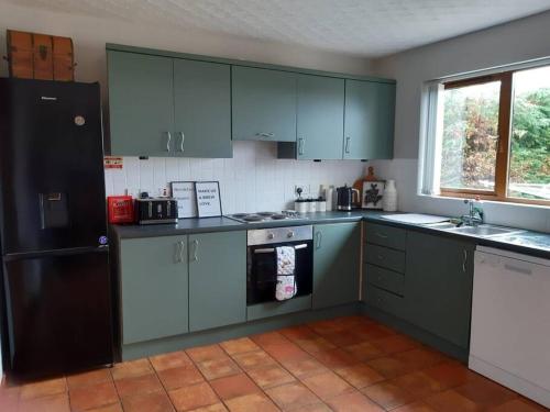 a kitchen with green cabinets and a black refrigerator at Whitepark Cottage - your home away from home in Ballycastle