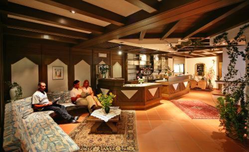 three people sitting on a couch in a living room at Hotel Garní Sunnleit´n in Monguelfo