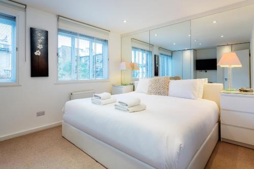 ein weißes Schlafzimmer mit einem großen weißen Bett und Fenstern in der Unterkunft Veeve - Village Virtuosity in London
