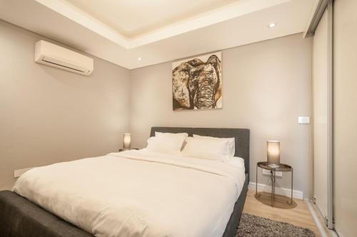 a bedroom with a white bed and a painting on the wall at Greenpoint Designer Apartment near Stadium & Waterfront in Cape Town