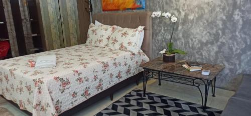Un dormitorio con una cama y una mesa con un arreglo floral. en Pousada Casa Bom Sono, en Foz do Iguaçu